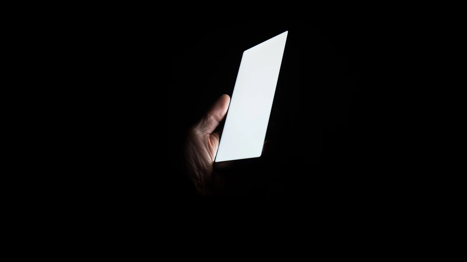 Karanlıkta parlayan boş ekranlı telefonu tutan bir el